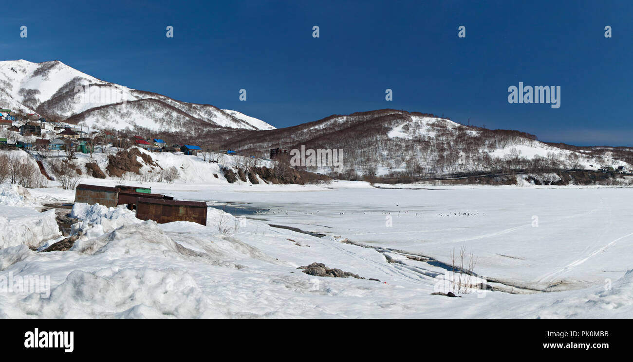 The frozen, thick ice-covered Babiya bay near snow-covered hills on a sunny winter day in Petropavlovsk-Kamchatsky, Russia Stock Photo