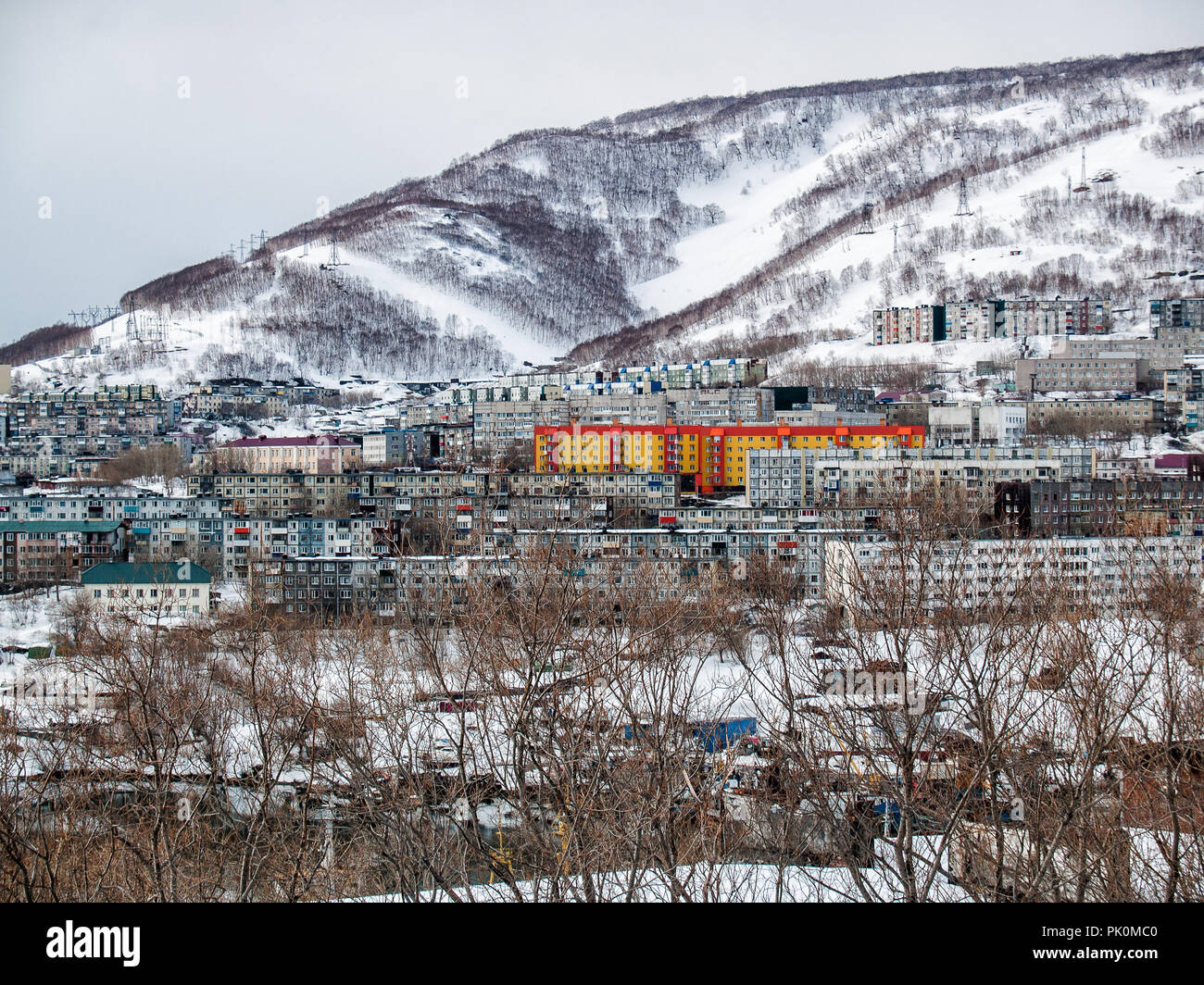 At the foot of the snow-covered hill with overgrown trees there are multi-storey houses in the winter on a sunny day in Petropavlovsk-Kamchatsky, Russ Stock Photo