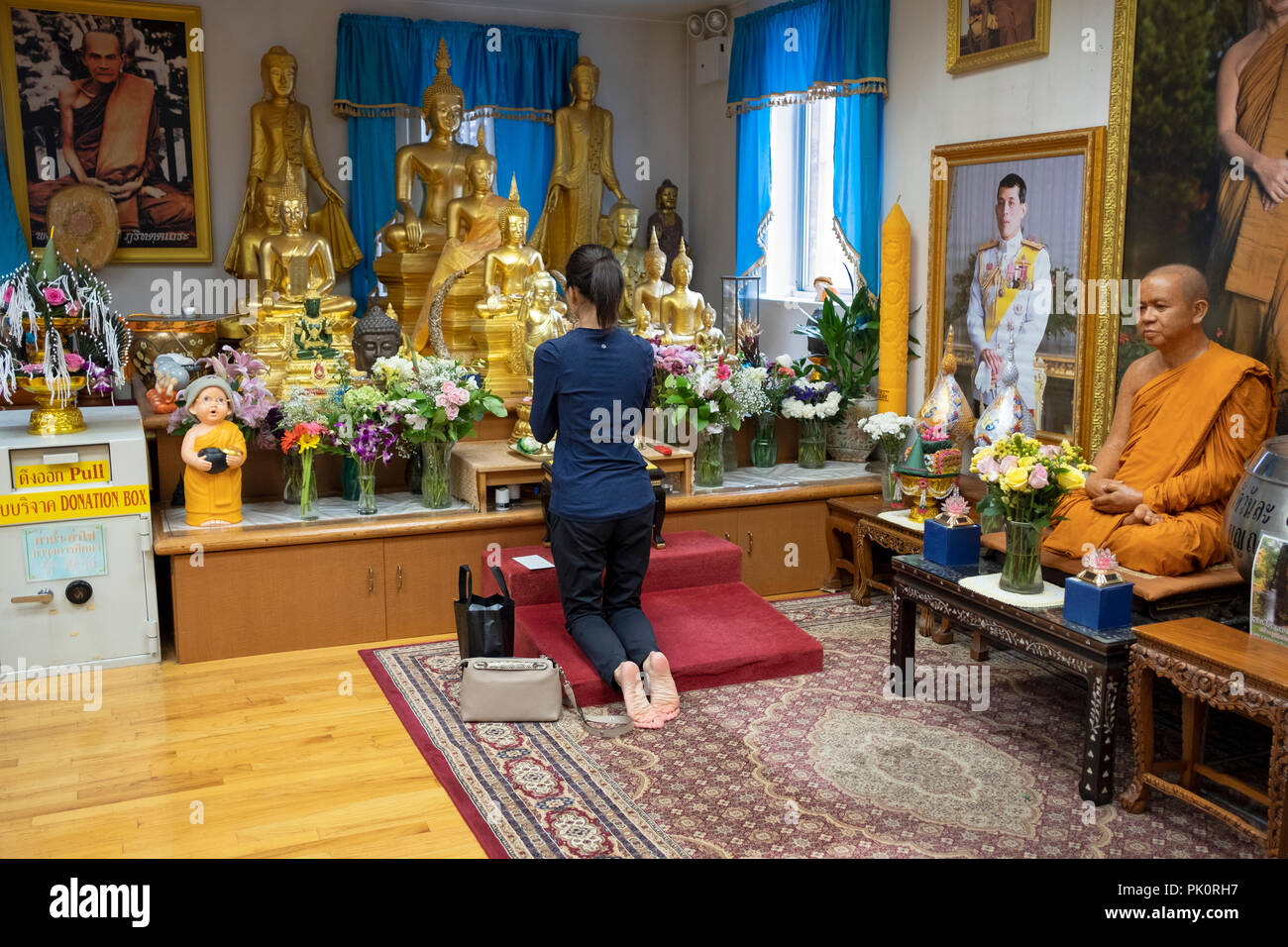 Unidentified woman worshipper kneeling in prayer & meditation in front of statues of Buddha at the Wat Buddah Thai Thavorn Vanaram in Elmhurst, Queens Stock Photo