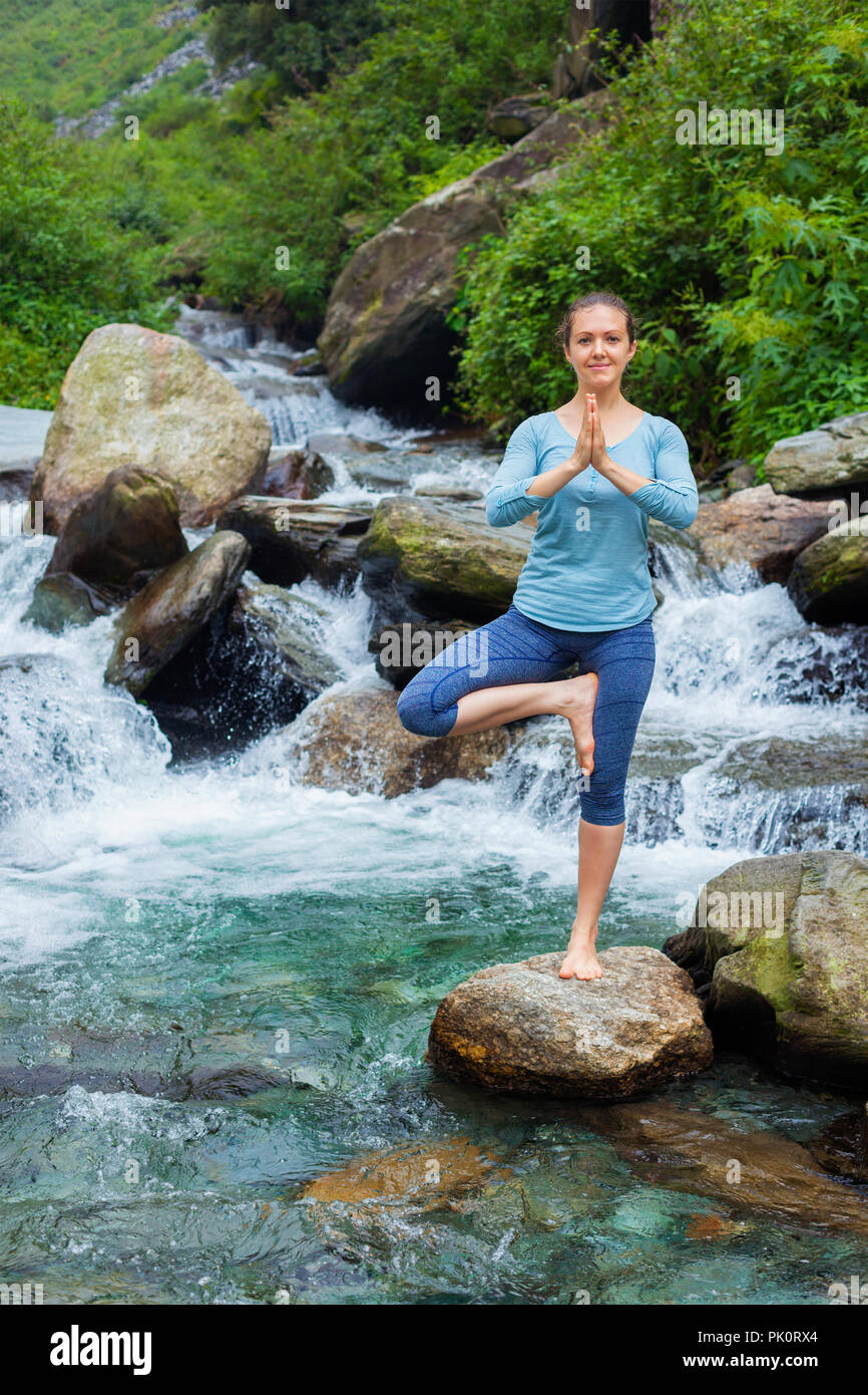 Woman in yoga asana Vrikshasana tree pose at waterfall outdoors Stock Photo