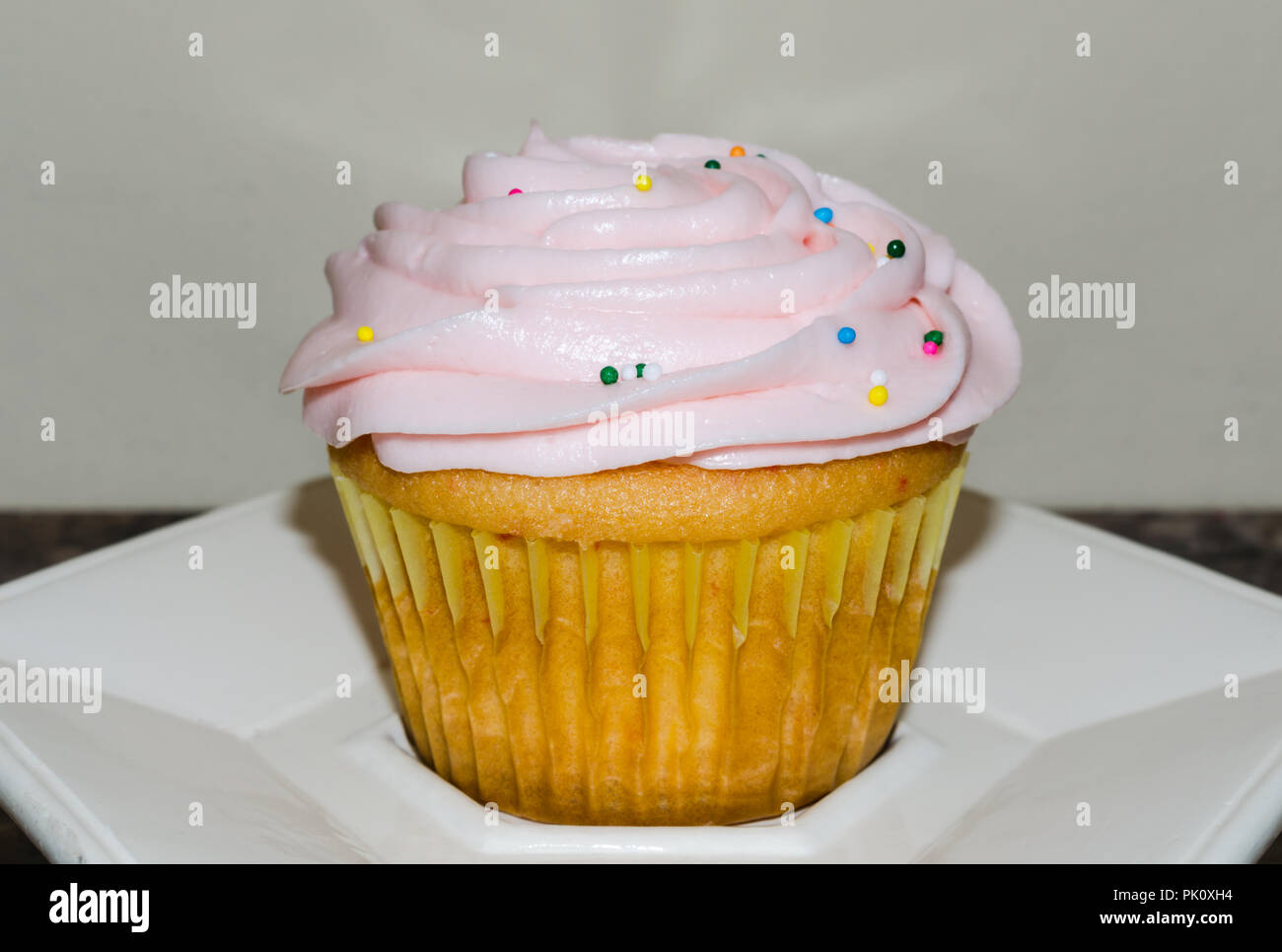 Light pink butter cream frosting swirled on top of fresh homemade cupcake. Colorful candy sprinkles sprinkled on top. Delicious sweet treat for party. Stock Photo