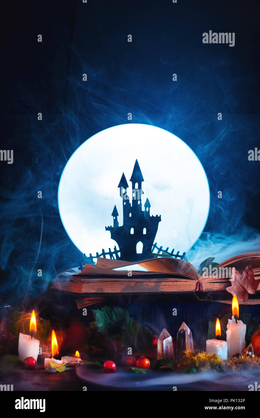 Halloween concept with a haunted castle silhouette in front of full Moon. Book of spells on witch or wizard workplace. Creative magical still life on  Stock Photo