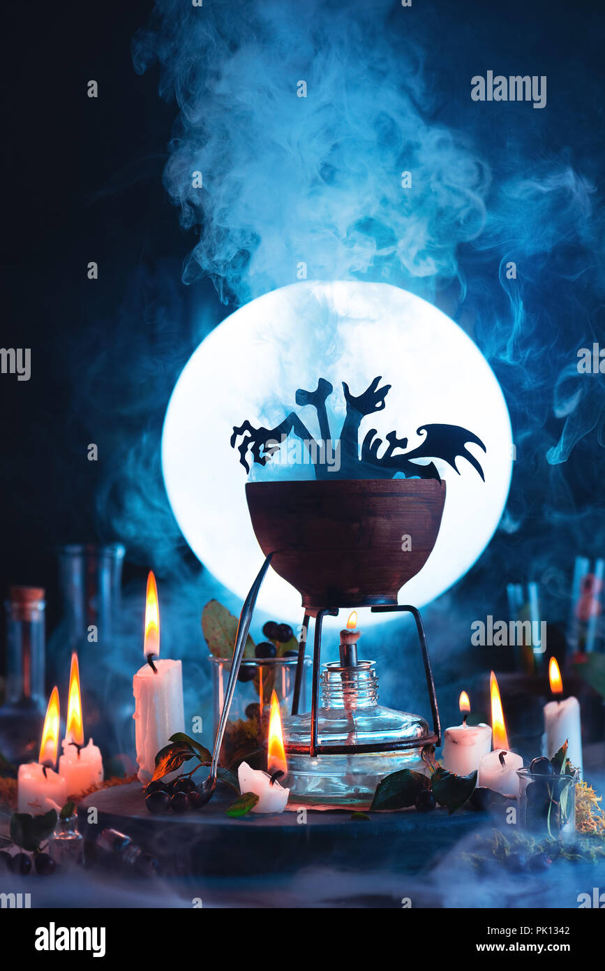 Halloween concept with a cauldron silhouette in front of full Moon. Magical potion with rising steam on witch or wizard workplace. Conceptual still li Stock Photo