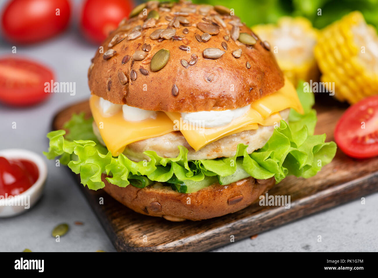 Chicken burger with cheese, lettuce and sauce on wooden serving board. Closeup view. Tasty juicy burger Stock Photo