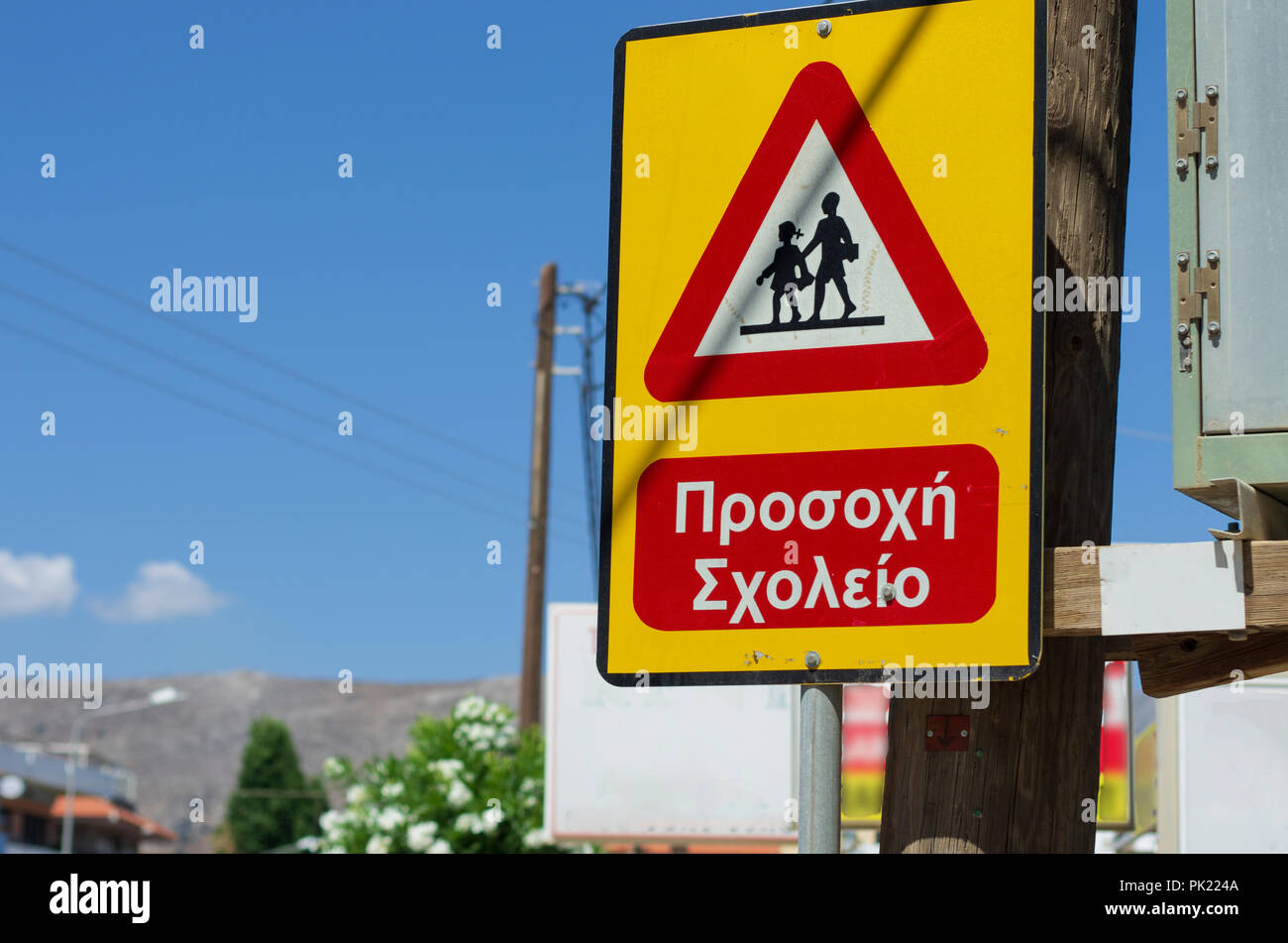 Triangle road sign 'Caution children' sunlit and greek inscription (no trade mark)  in Greece Stock Photo