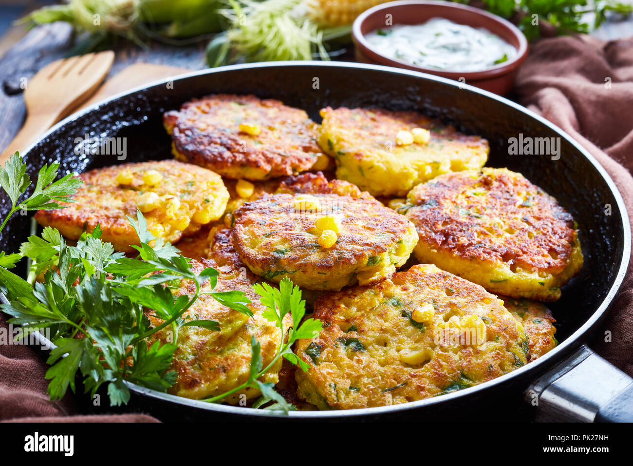 fried corn fritters in a skillet with yogurt dipping sauce and fresh