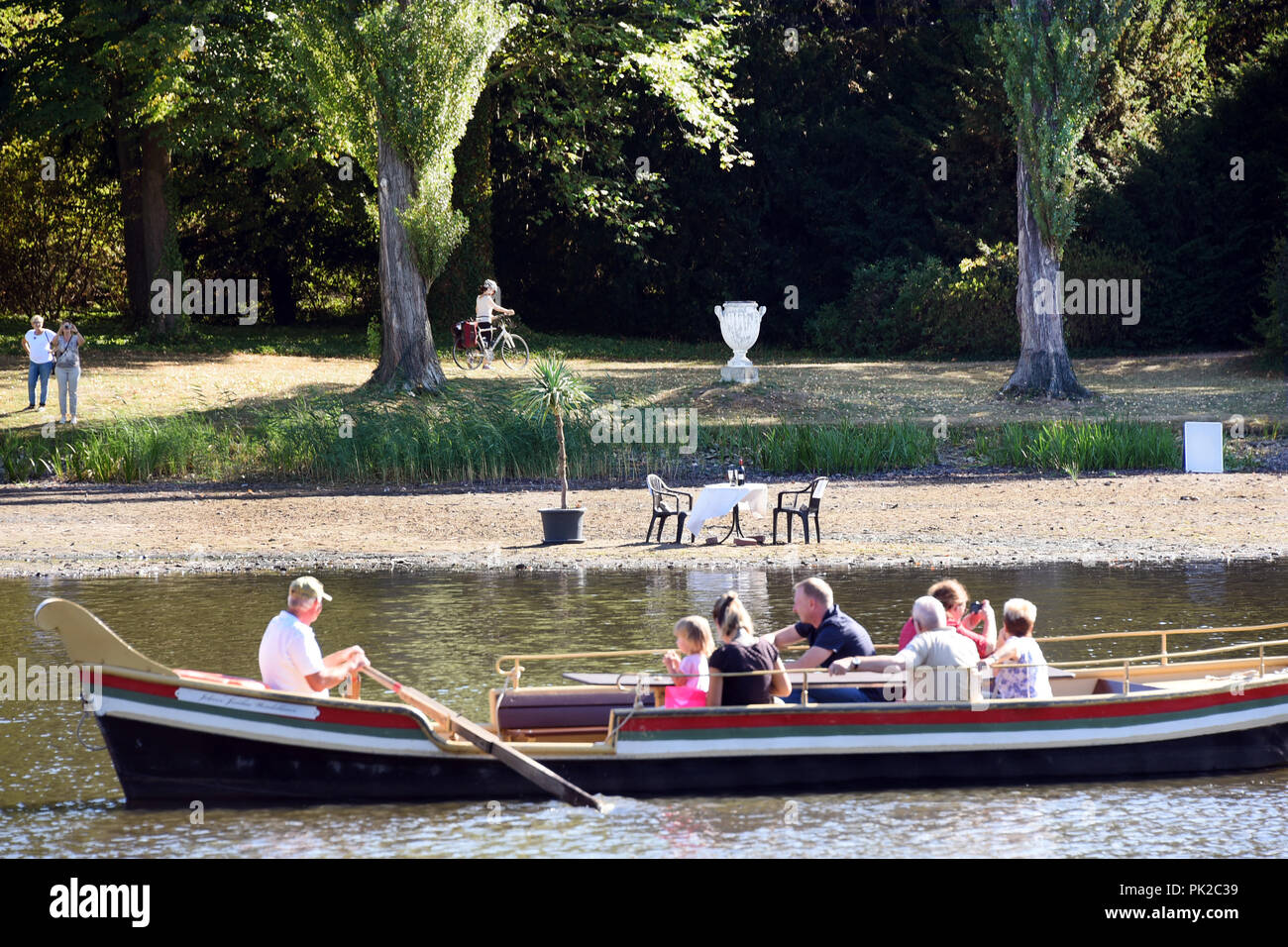09.09.2018, Saxony-Anhalt, Wörlitz: A gondola runs along the sandbank, otherwise covered with about one meter of water, in the Wörlitz Garden Kingdom, on which the gondoliers have placed a table set in white and two chairs. The gondoliers, who are no longer able to navigate the canals with the visitors, but can use part of the lake, want to embellish the dried out peripheral areas with their installation. The drought, which has lasted for months, has drained almost the entire extensive canal system in the Wörlitz Garden Kingdom, a UNESCO World Heritage Site. The landscape park between Dessau-R Stock Photo