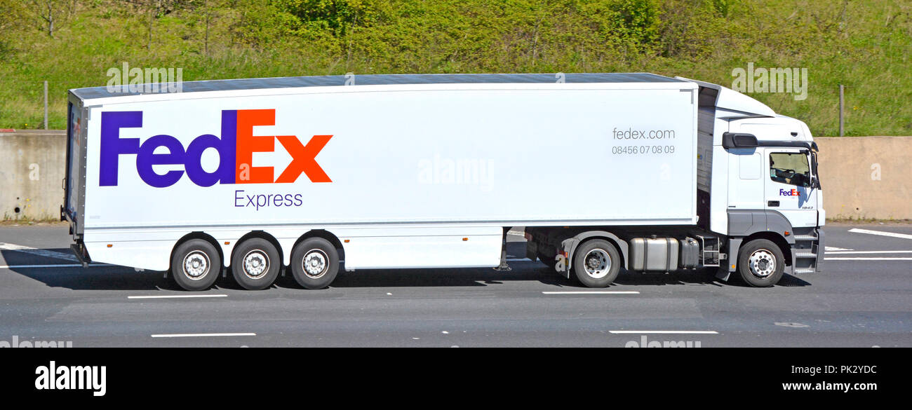 Side view FedEx Express transport delivering packages & freight via hgv lorry truck articulated white trailer & logo driving along motorway England UK Stock Photo