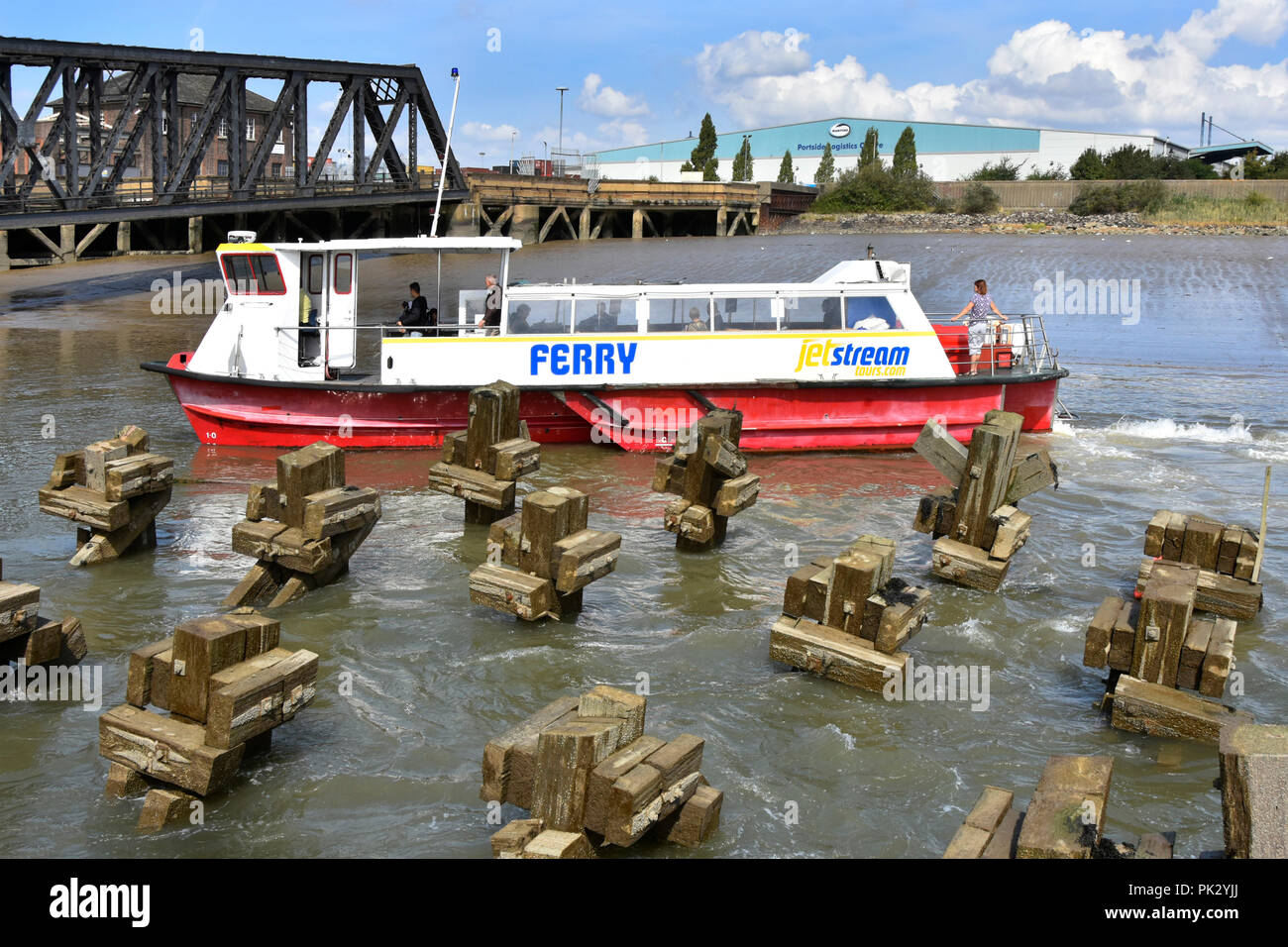 Thames passenger ferry boat from Gravesend Kent navigating obstruction exposed by low tide beside Tilbury landing stage & road bridge Essex England UK Stock Photo