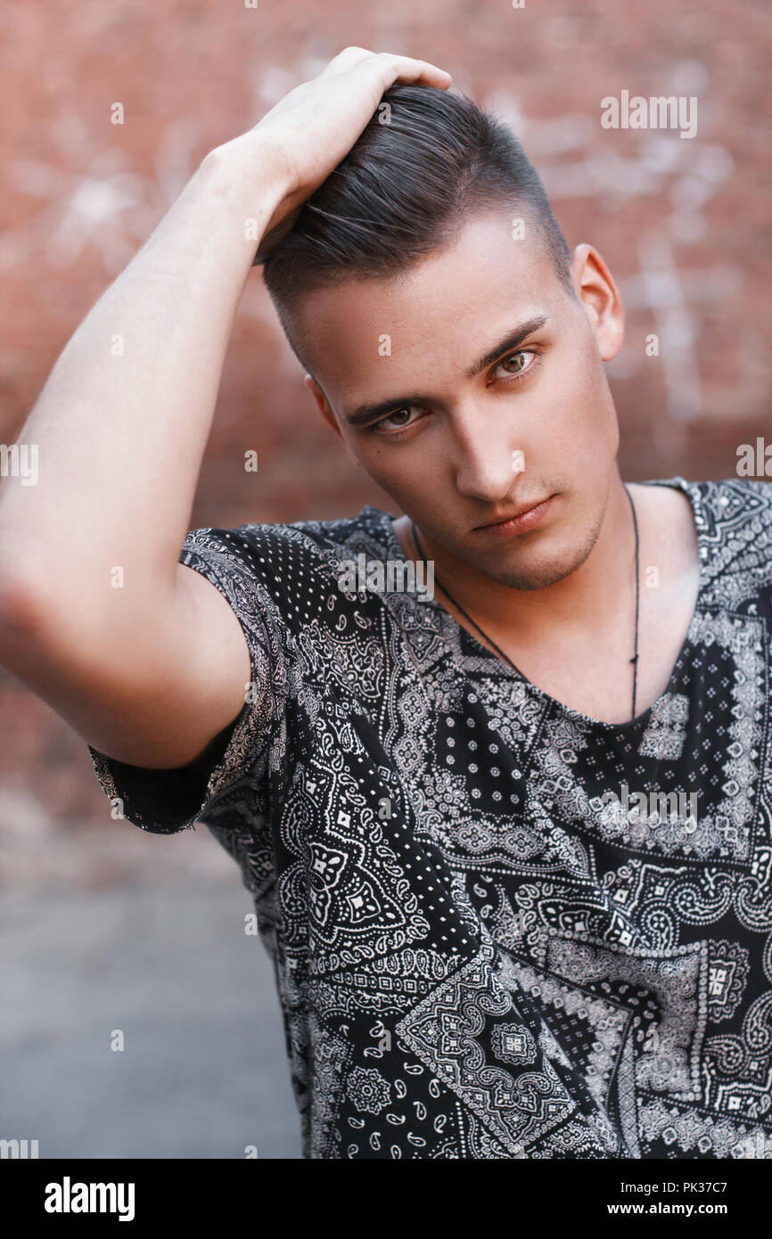 Close-up portrait of a young hipster in a black vintage t-shirt on a background of red bricks. Stock Photo