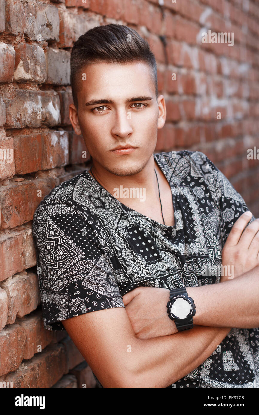 Handsome young guy from America stands on the brick wall background. Stock Photo