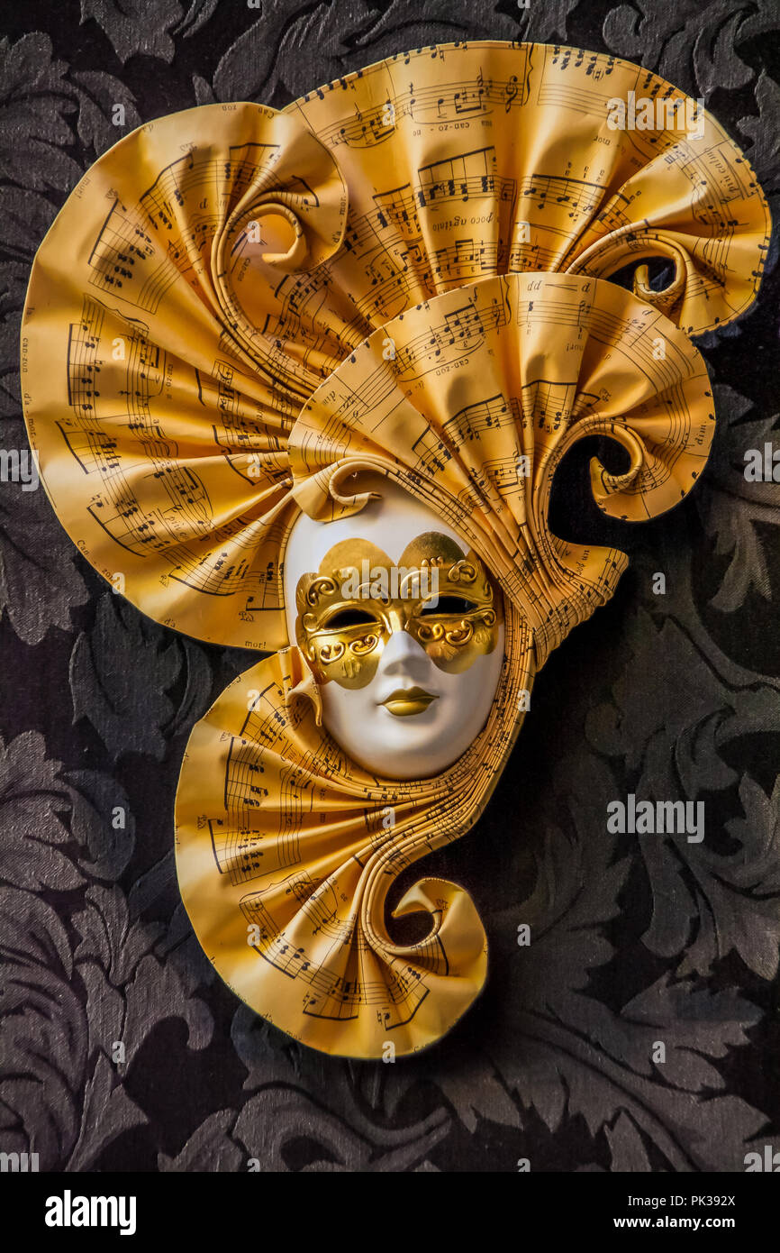 A golden Venetian mask, with decorative swirls with a music motif. Stock Photo