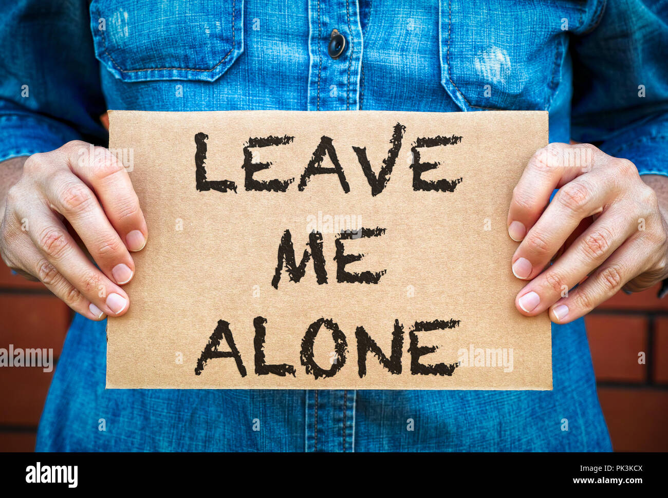 Woman hands holding piece of cardboard with words Leave Me Alone ...