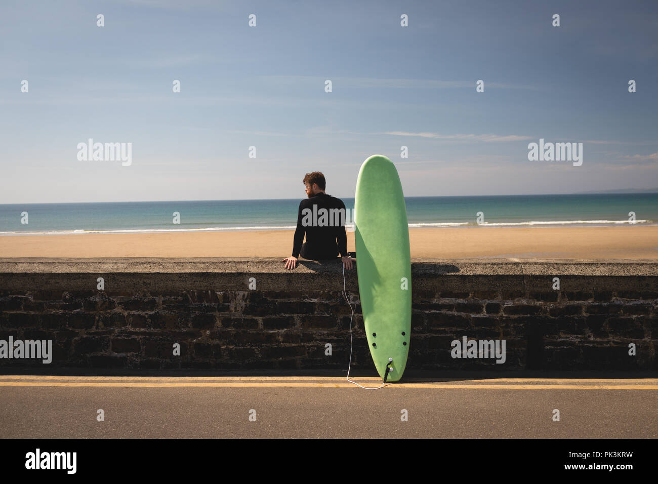 Surfer with surfboard sitting on surrounding wall Stock Photo