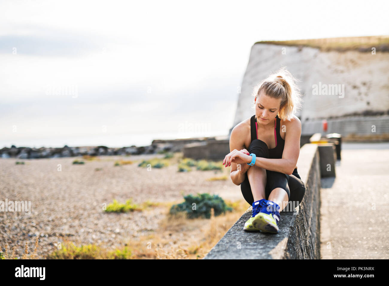 Young sporty woman runner resting outside in nature, setting smartwatch. Stock Photo