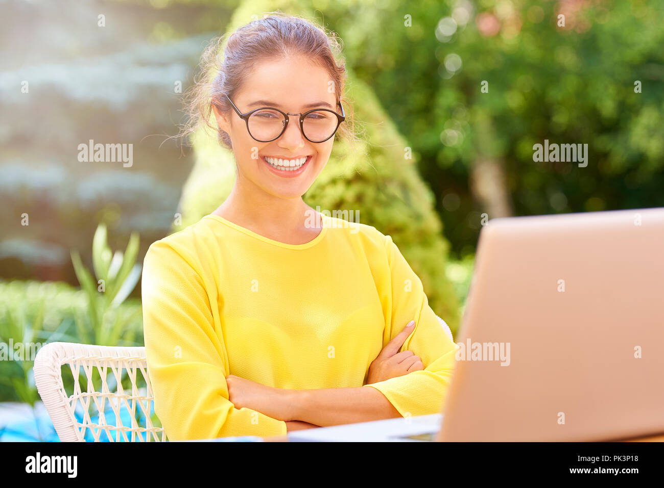 Portrait of relaxed young woman sitting with folded arms outdoor behind her laptop while working on her presentation. Stock Photo