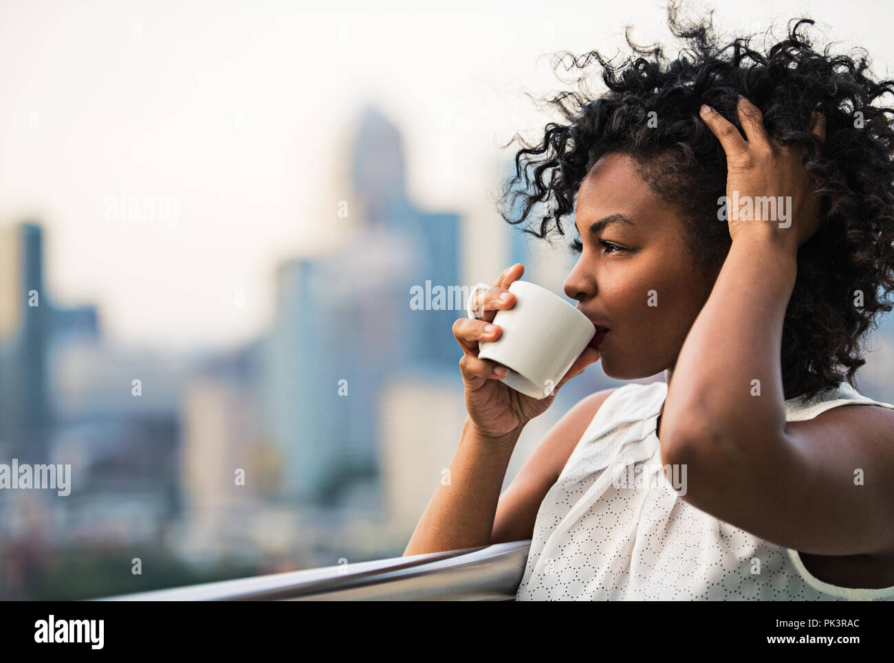 A close-up portrait of a woman standing on a terrace, drinking coffee. Stock Photo