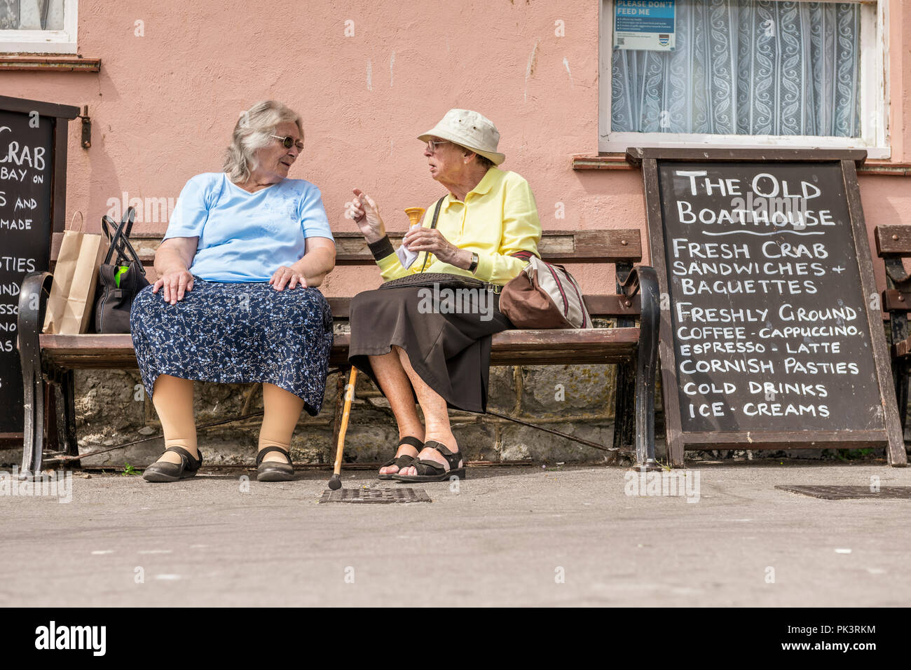 Two ladies are deep in conversation on a bench whilst enjoying the sunshine at the seafront in Lyme Regis in West Dorset. Stock Photo