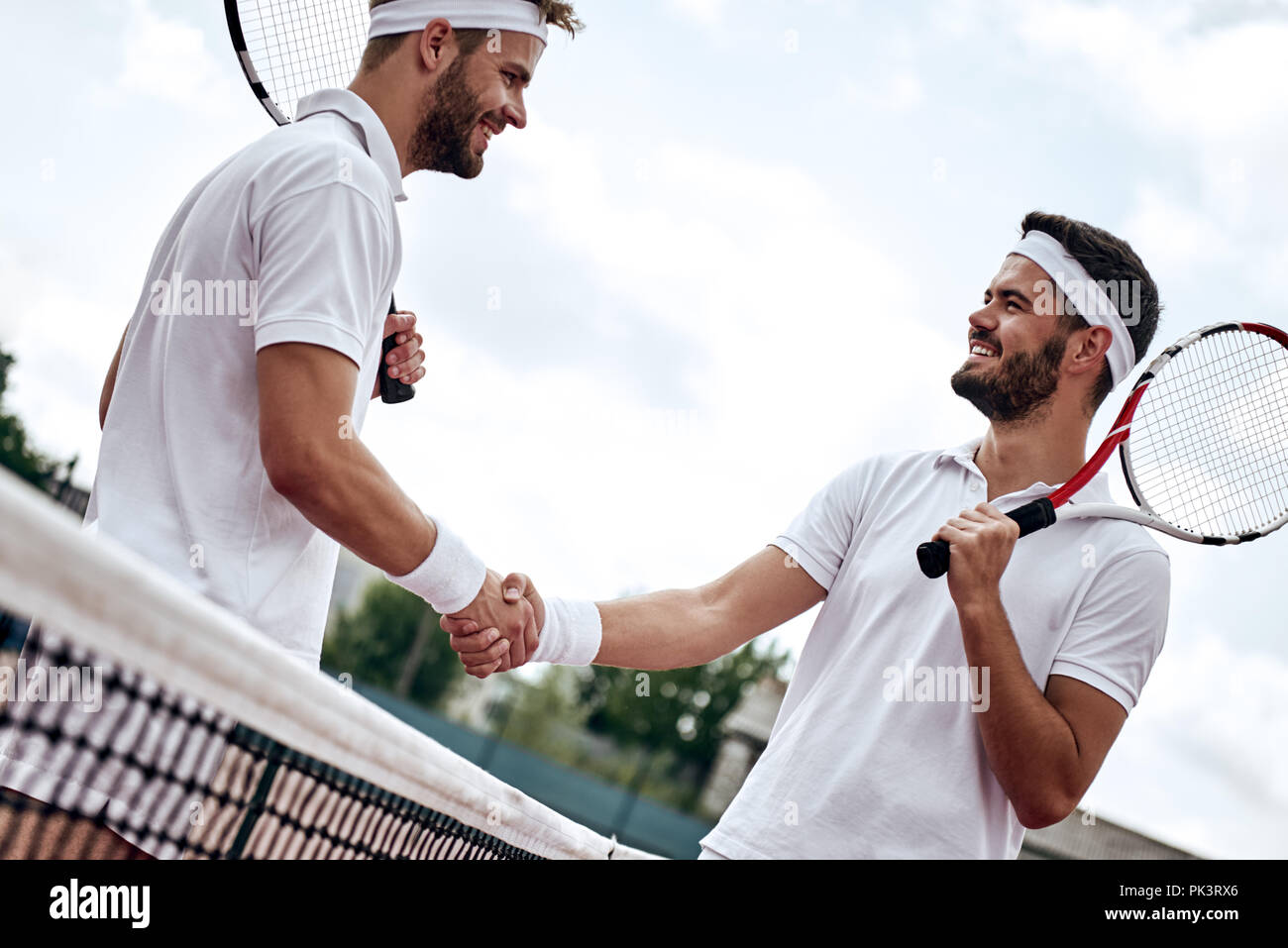 Two men, professional tennis players shake hands before and after the tennis match. One of they has the face of anger. He is trying to intimidate his opponent. Stock Photo