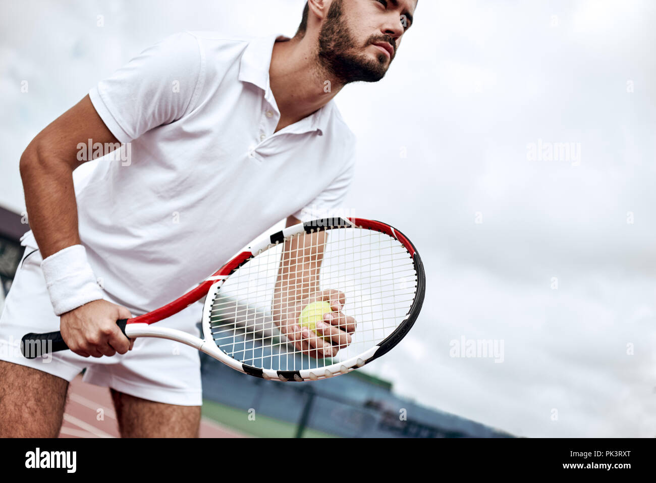 Professional tennis player man athlete waiting to receive ball, playing game on hard court. Fitness person focused behind net ready to return training cardio on outdoor sport activity. Stock Photo