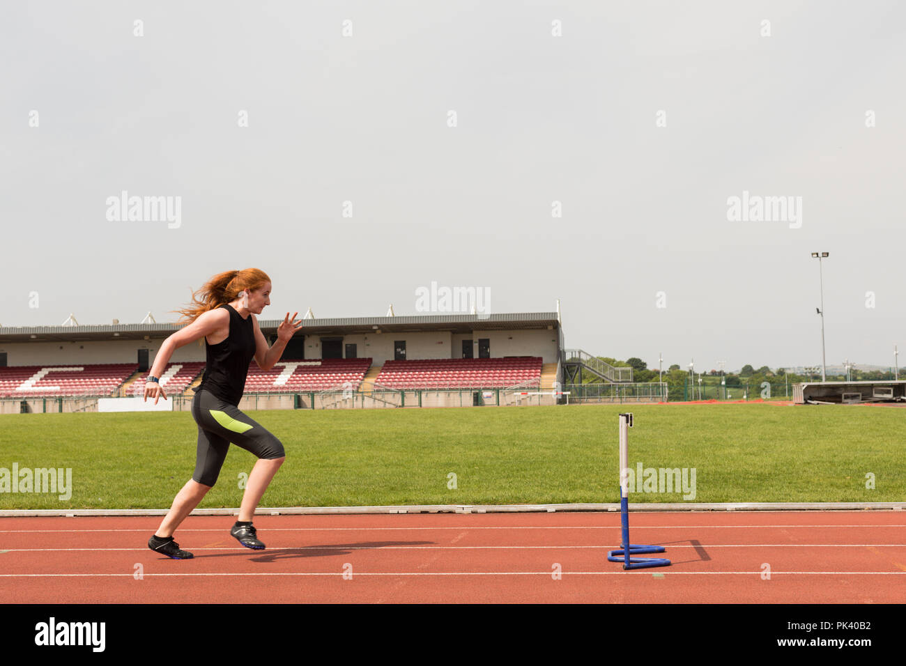 Female athletic running over hurdle on sports track Stock Photo