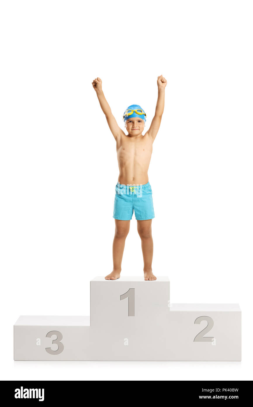 Full length portrait a happy boy in swimming trunks standing on a winners pedestal holding his hands up isolated on white background Stock Photo