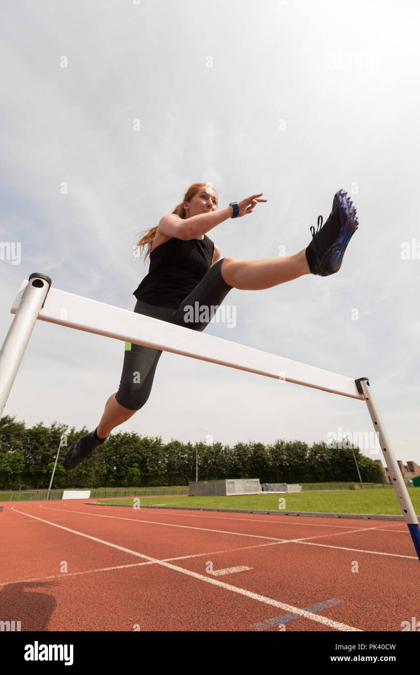Female athletic jumping over hurdle on sports track Stock Photo
