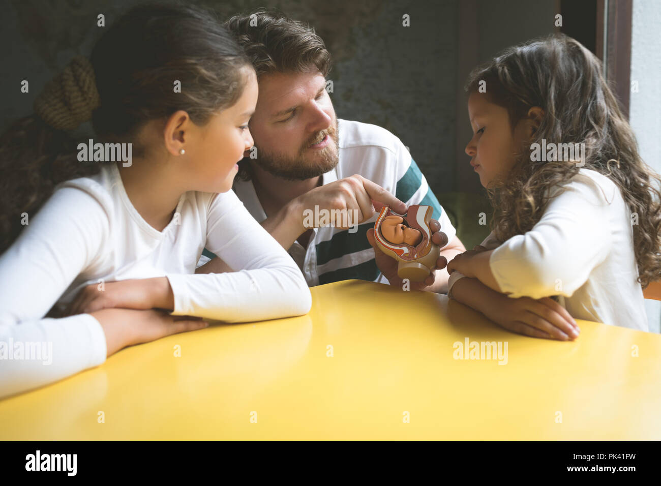 Father explaining his daughters about fetus model Stock Photo