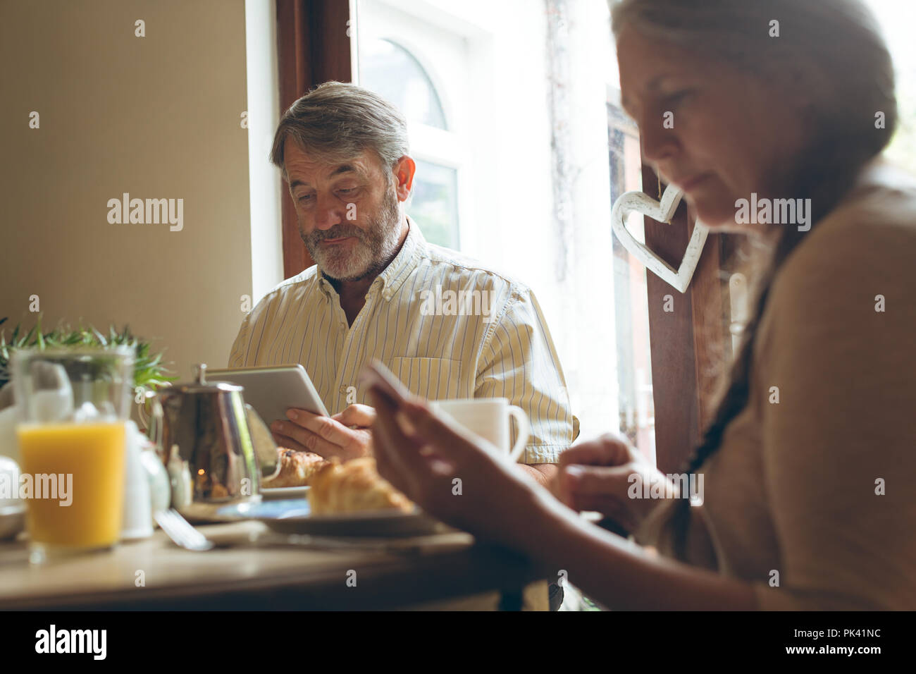 Senior couple using digital tablet and mobile phone while having breakfast Stock Photo
