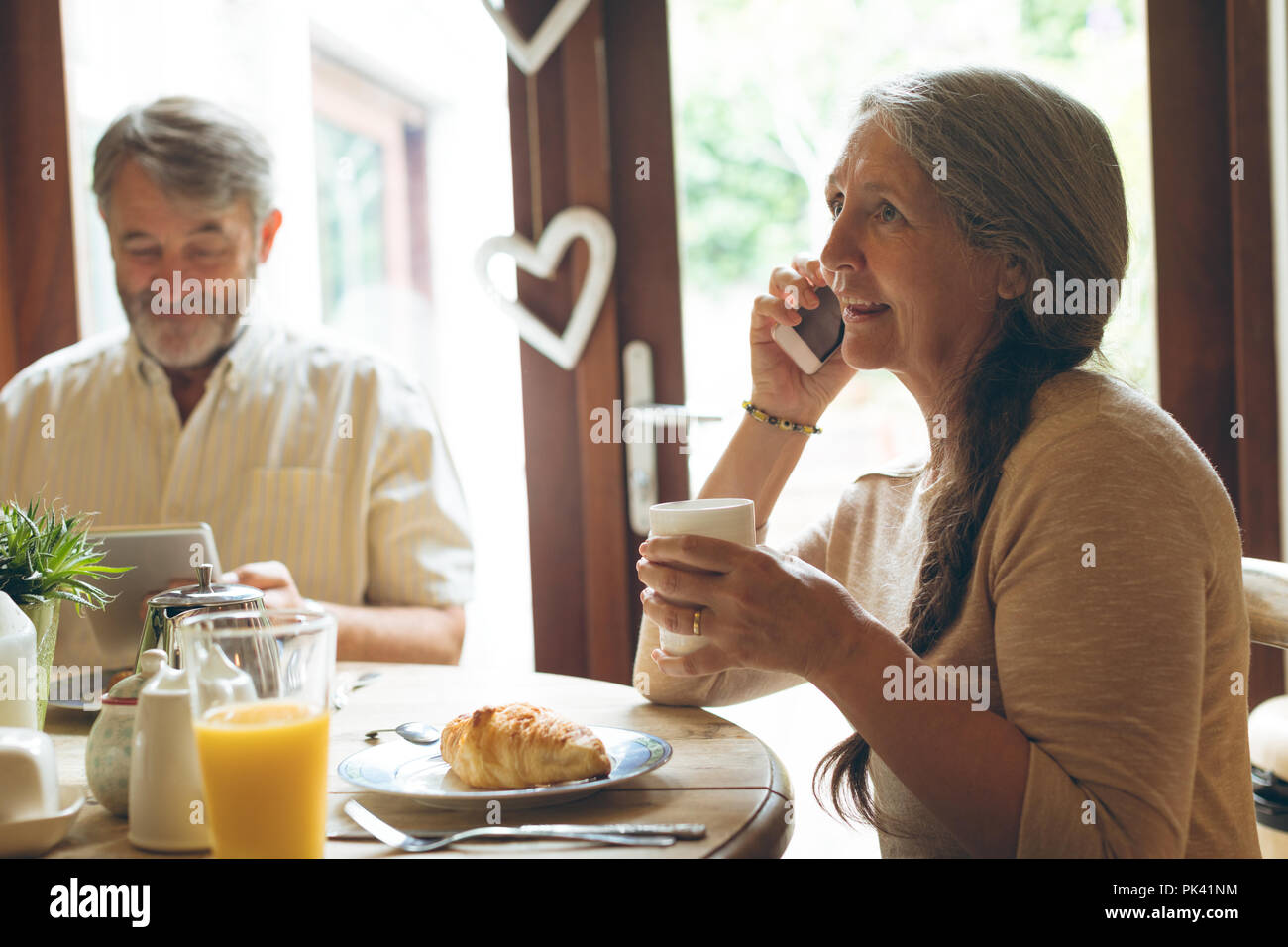 Senior woman talking on mobile phone while having coffee Stock Photo