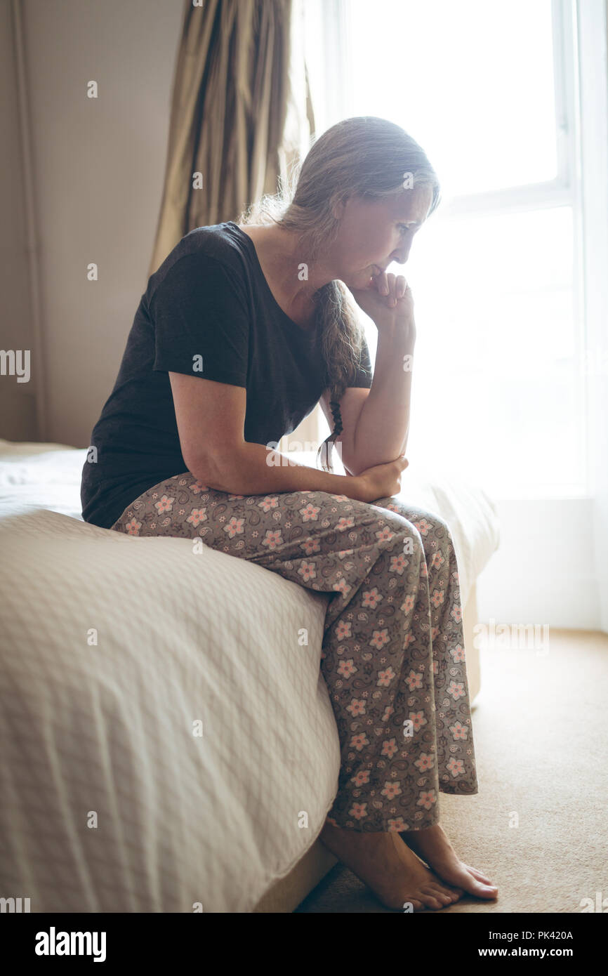 Senior woman sitting on bed in bedroom at home Stock Photo