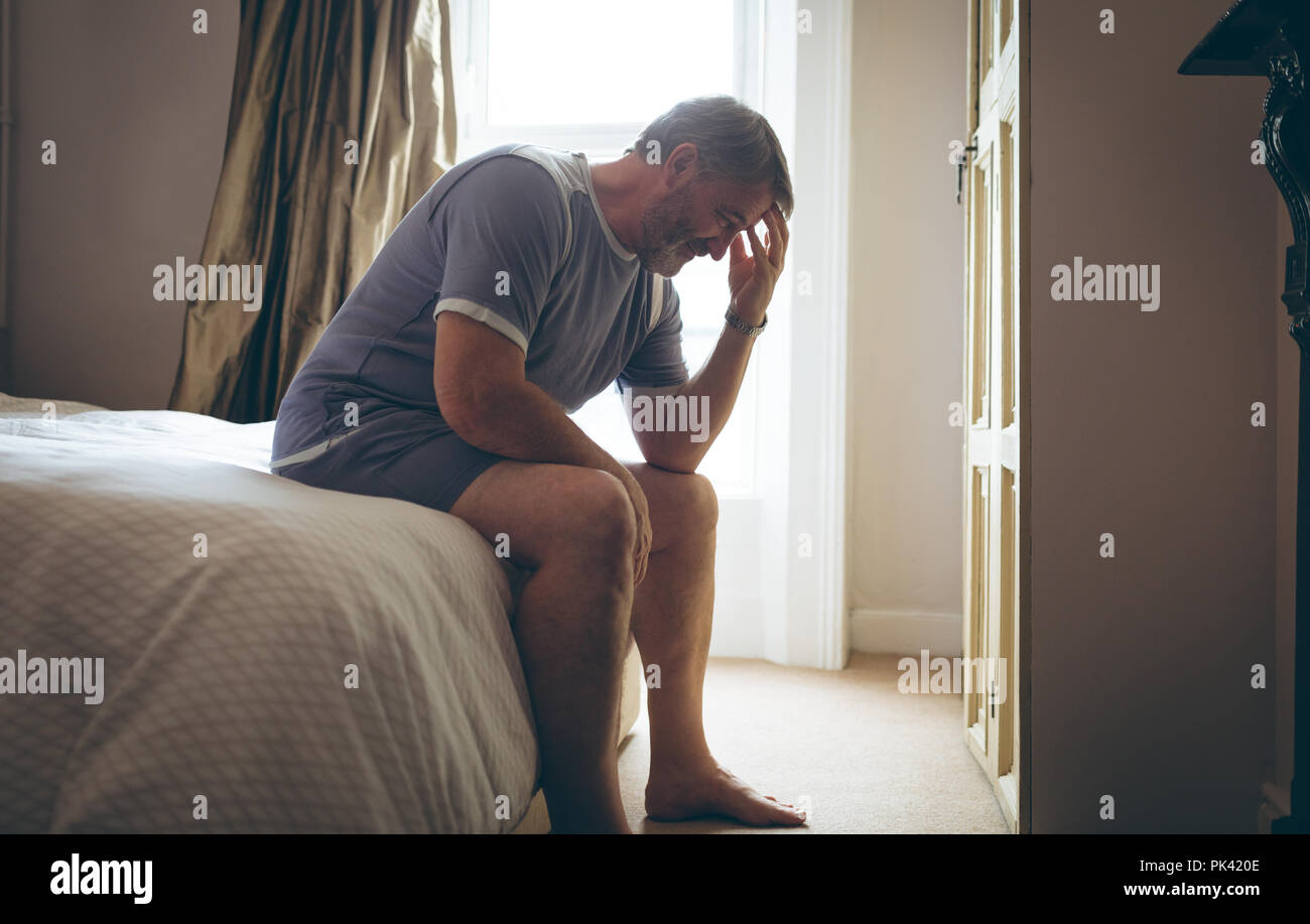 Senior man sitting on bed in bedroom at home Stock Photo