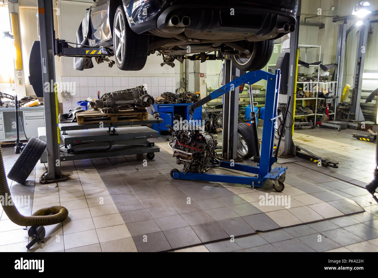 A sports car raised on a lift for repair and under it a detached engine ...