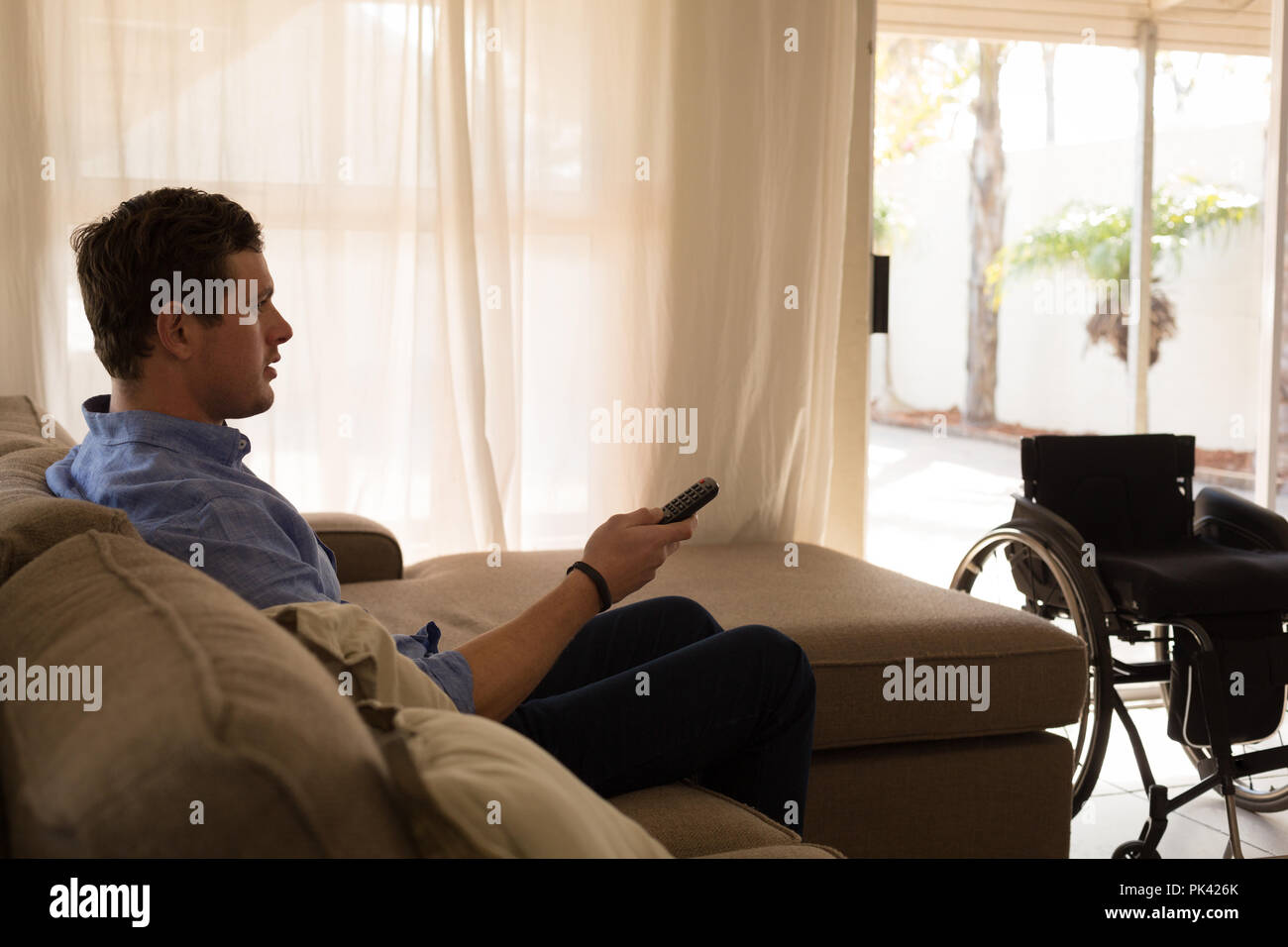 Disabled man changing channels in living room Stock Photo