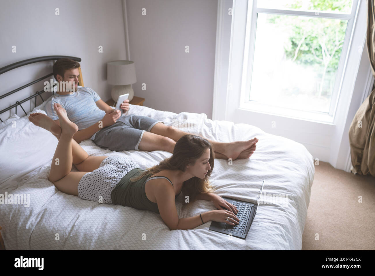 Couple using laptop and digital tablet in bedroom Stock Photo