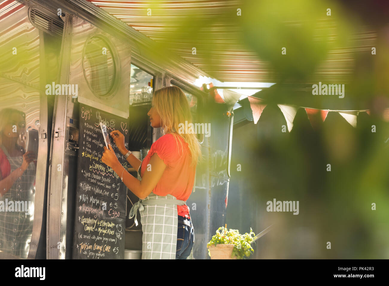 Female waitress writing menu on menu board while using digital tablet Stock Photo