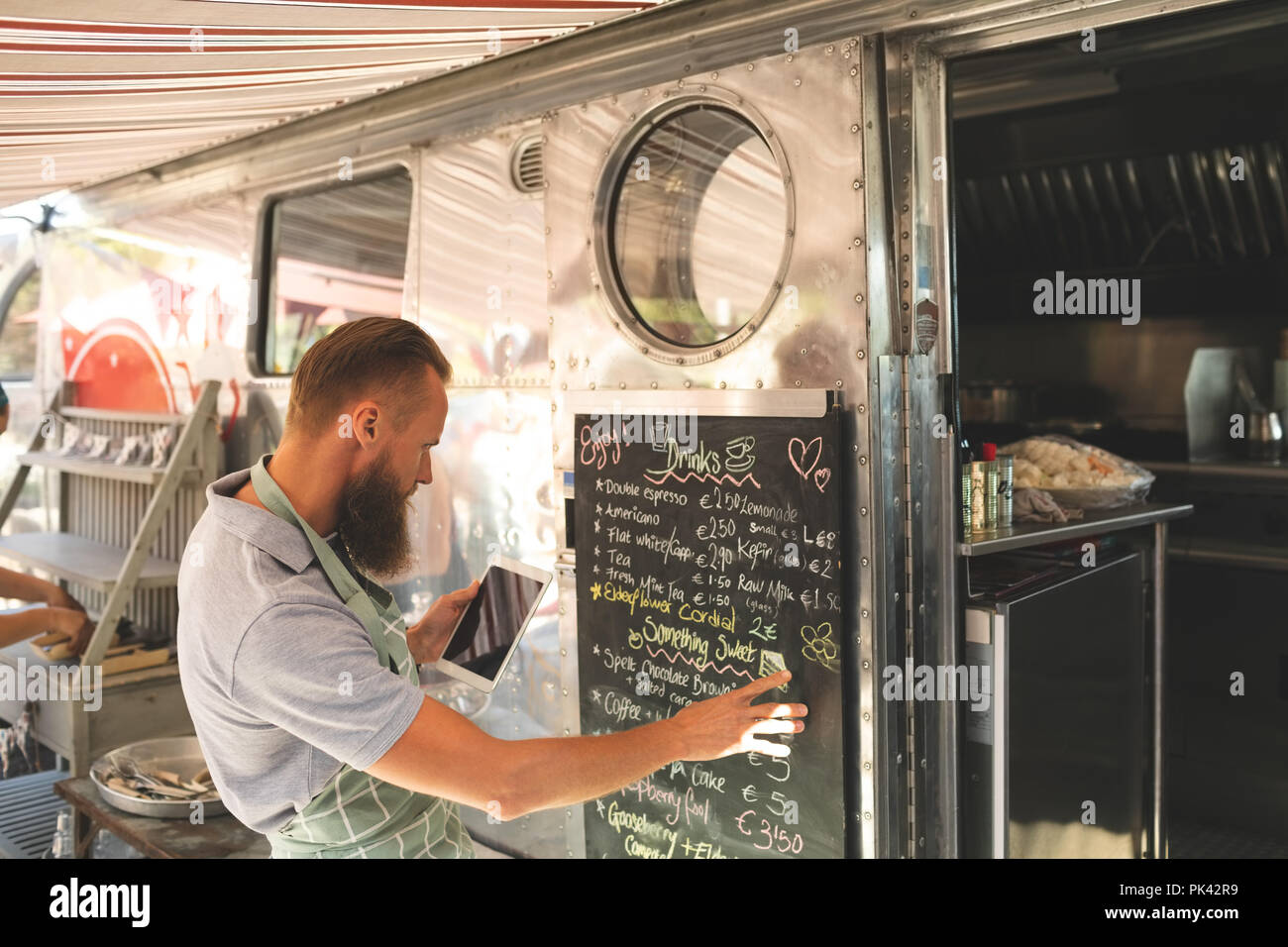 Male waitress writing menu on menu board while using digital tablet Stock Photo