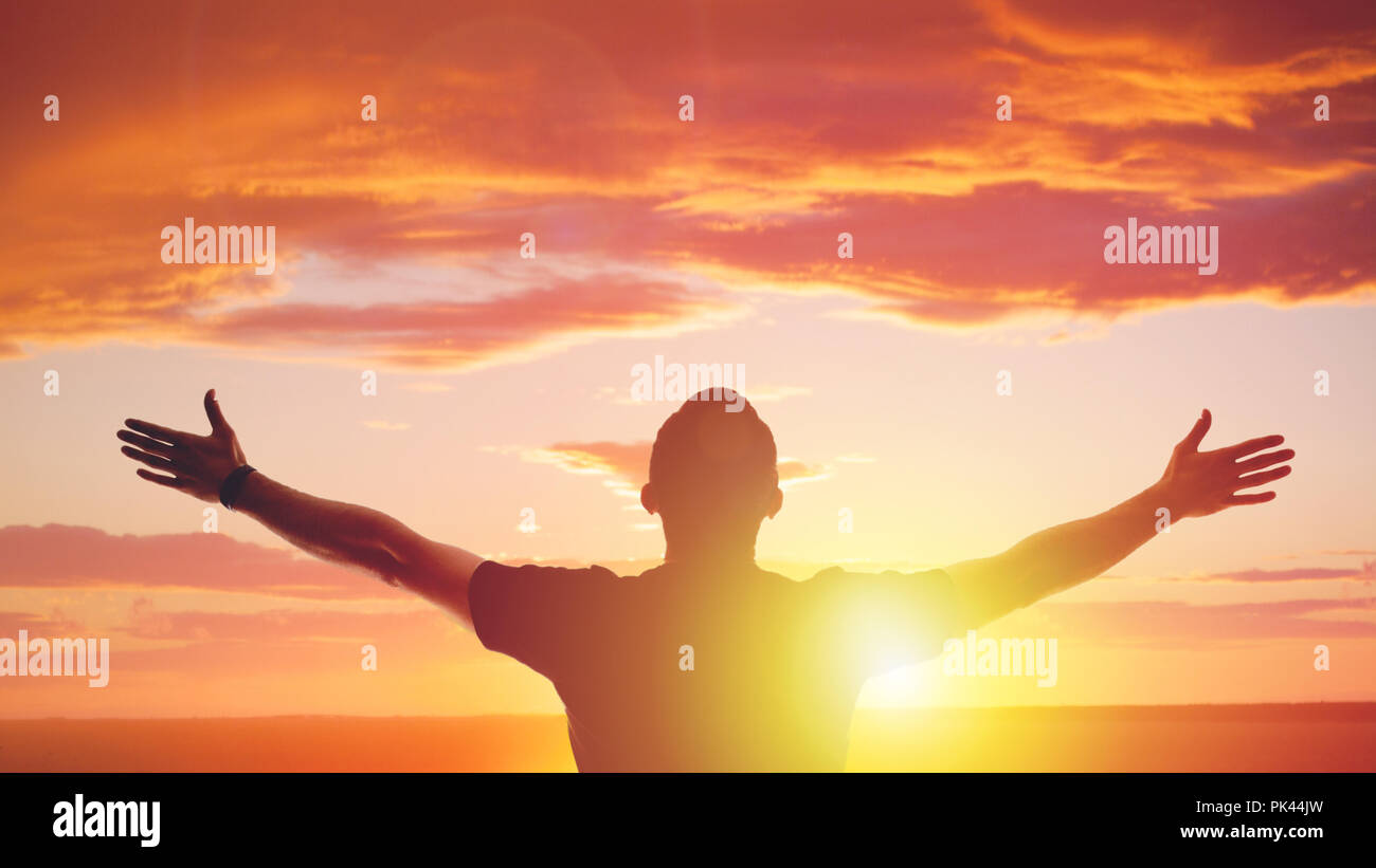 Young man standing outstretched at sunset. Bright solar glow and sky Stock Photo