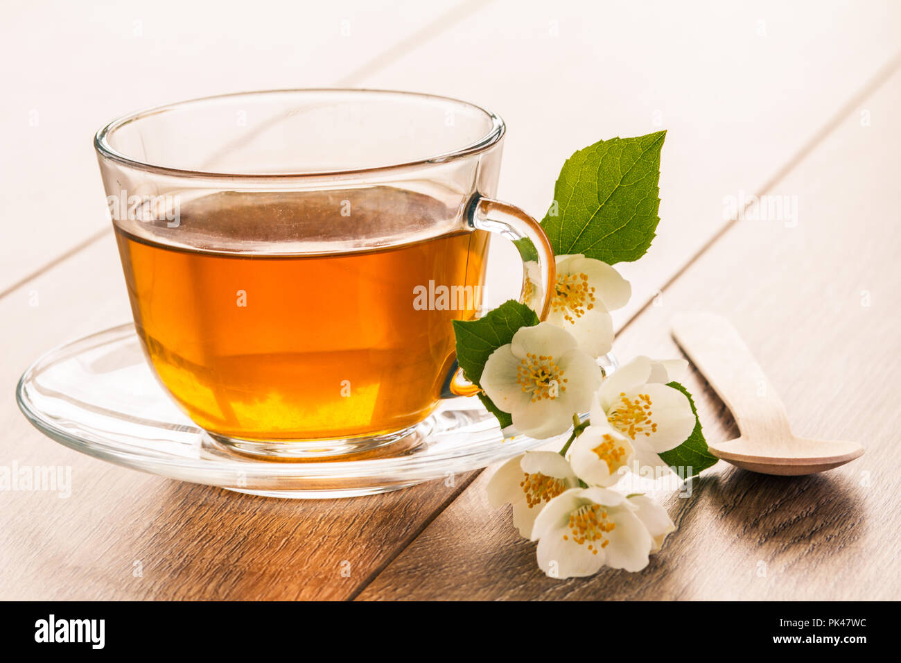 Glass cup of green tea with white jasmine flowers on wooden background