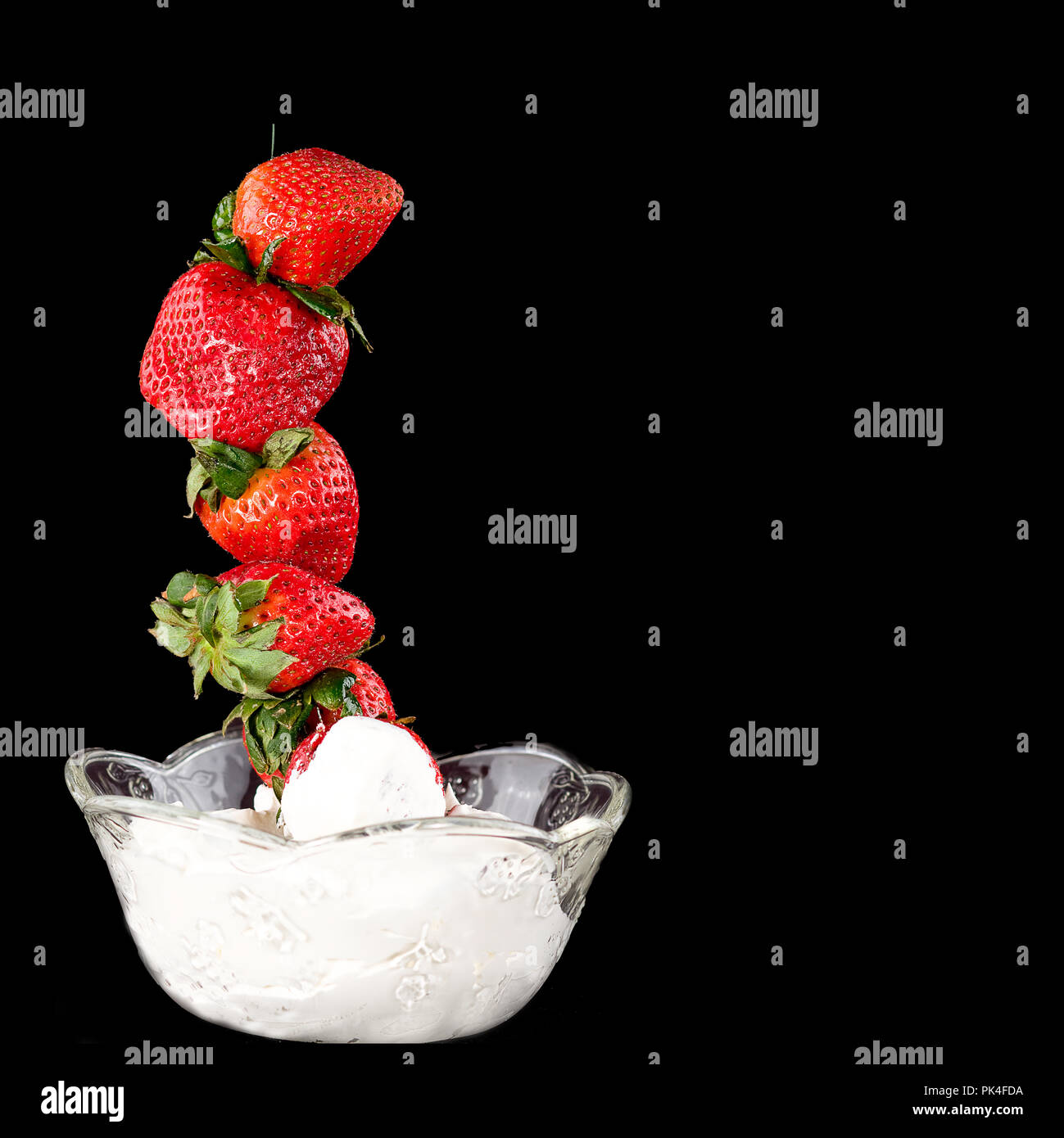 Strawberries stacked high out of a dish of whipped cream in this concept image isolated on black background. Stock Photo