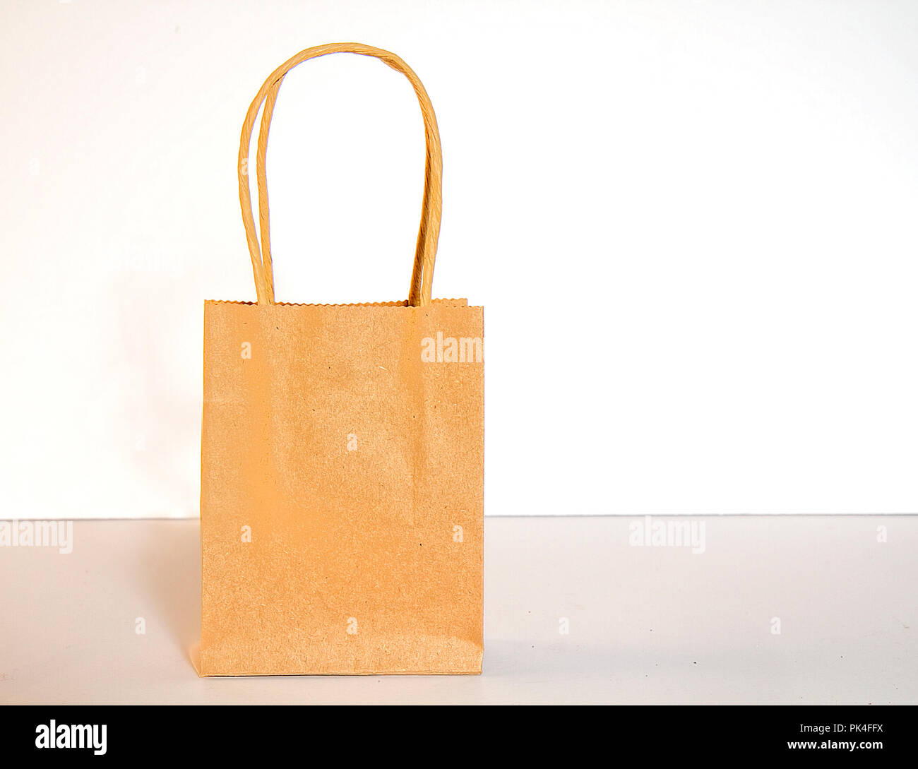 Small brown paper shopping bag with handles isolated on white background. Stock Photo