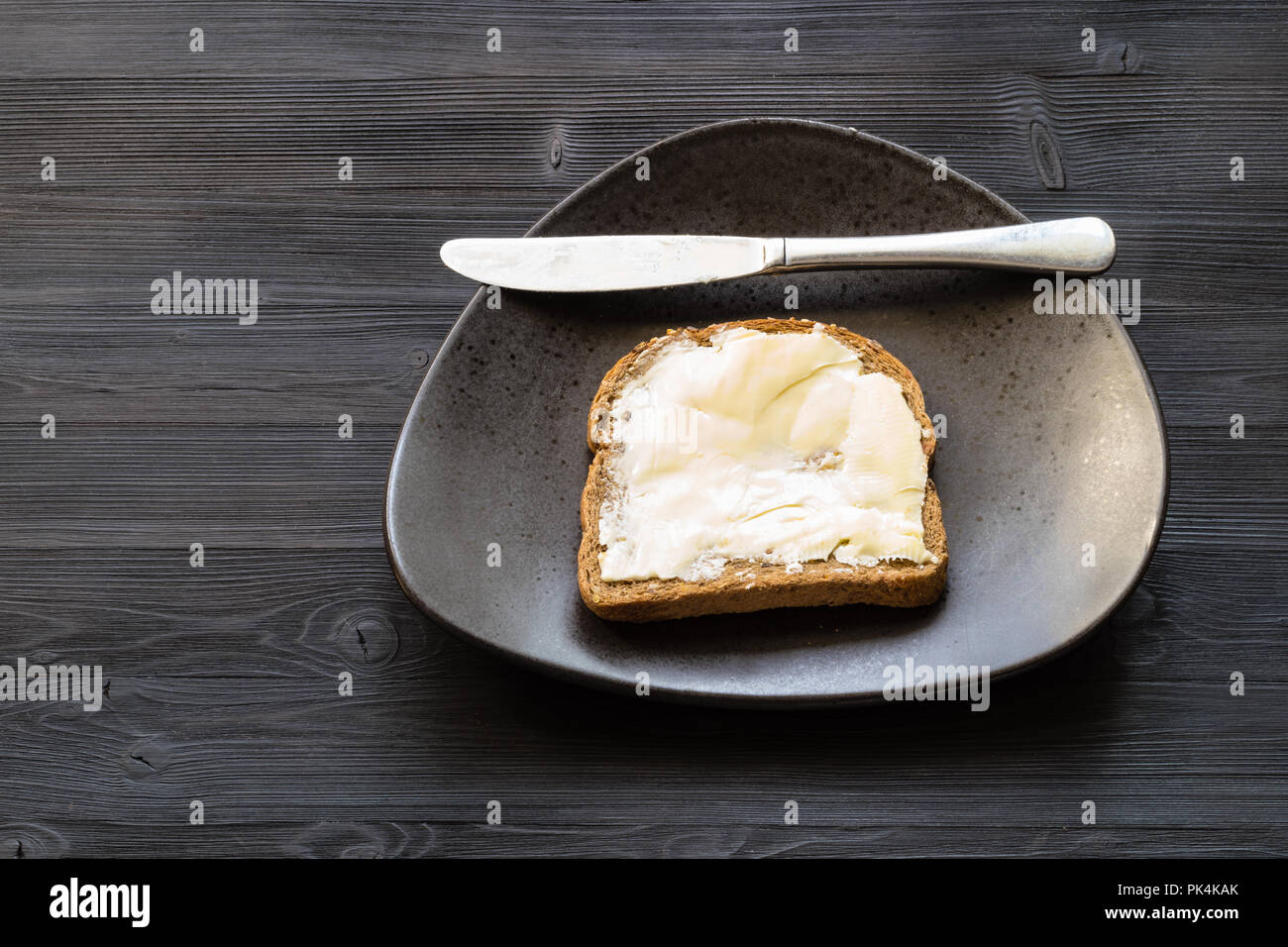 bread sandwich with buttered butter and knife on black plate on dark wooden table with blank copyspace Stock Photo