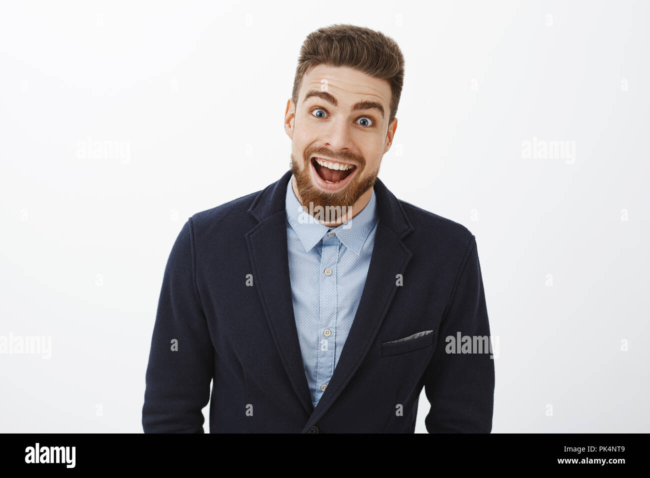 Waist-up shot of enthusiastic delighted and surprised charismatic young rich bachelor in stylish suit with beard and blue eyes smiling broadly from amazement and joy gazing impressed at camera Stock Photo