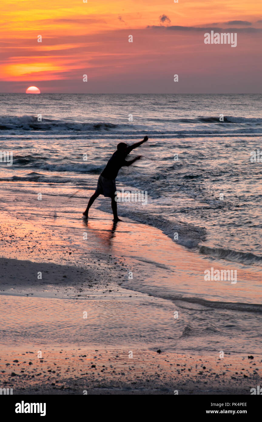 A silhouette of a man throwing a cast net for bait fish with the