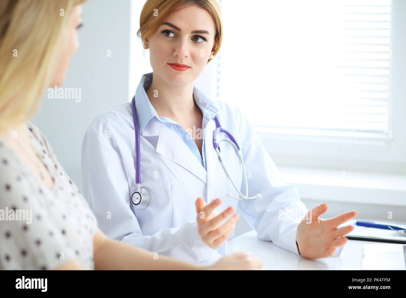 Doctor and patient discussing something while sitting at the desk at ...