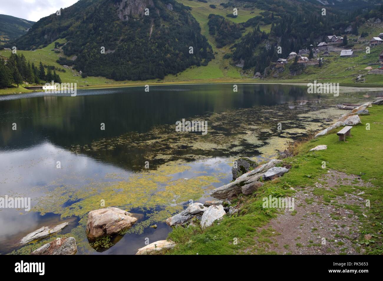 Scenery image view of mountain lake and wooden shepherd huts with view of sky and forest in the background Stock Photo