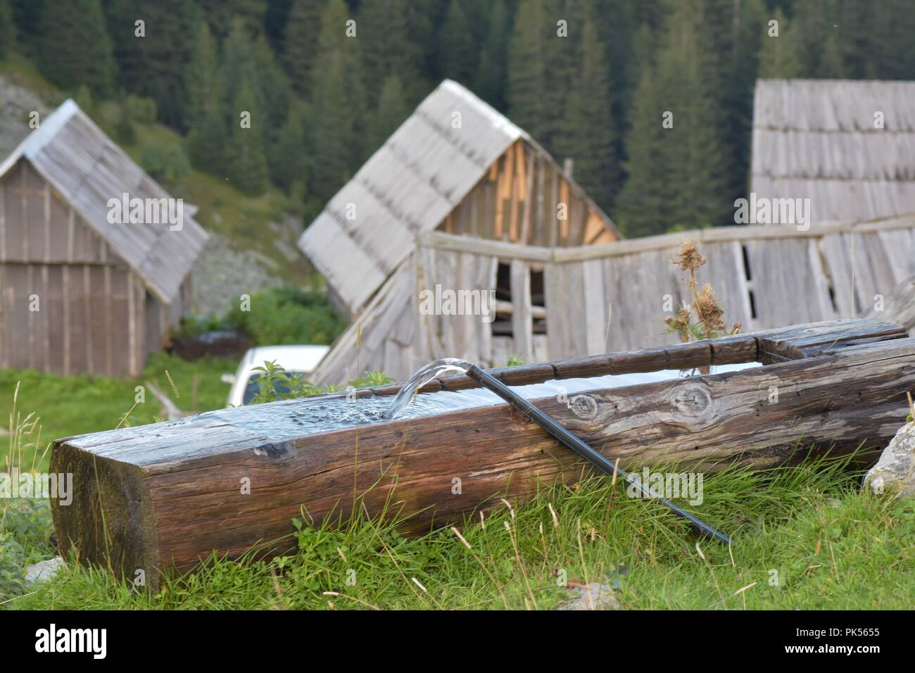 Flowing water in wood log made basin with mountain landscape in background Stock Photo
