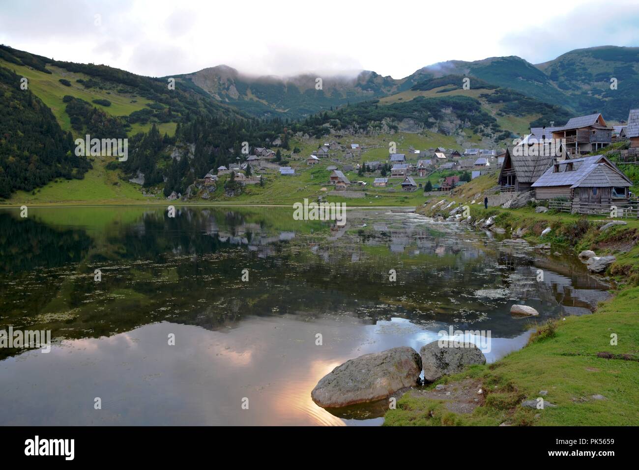 Scenery image view of mountain lake and wooden shepherd huts with view of sky and forest in the background Stock Photo