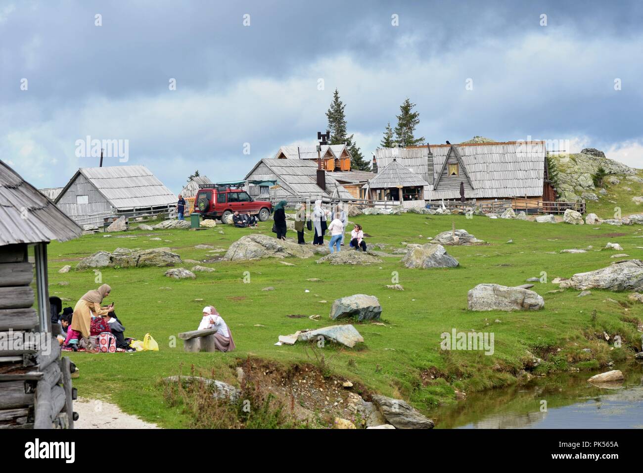 Scenery image view of green valley with group of people and wooden shepherd huts with view of sky in the background Stock Photo