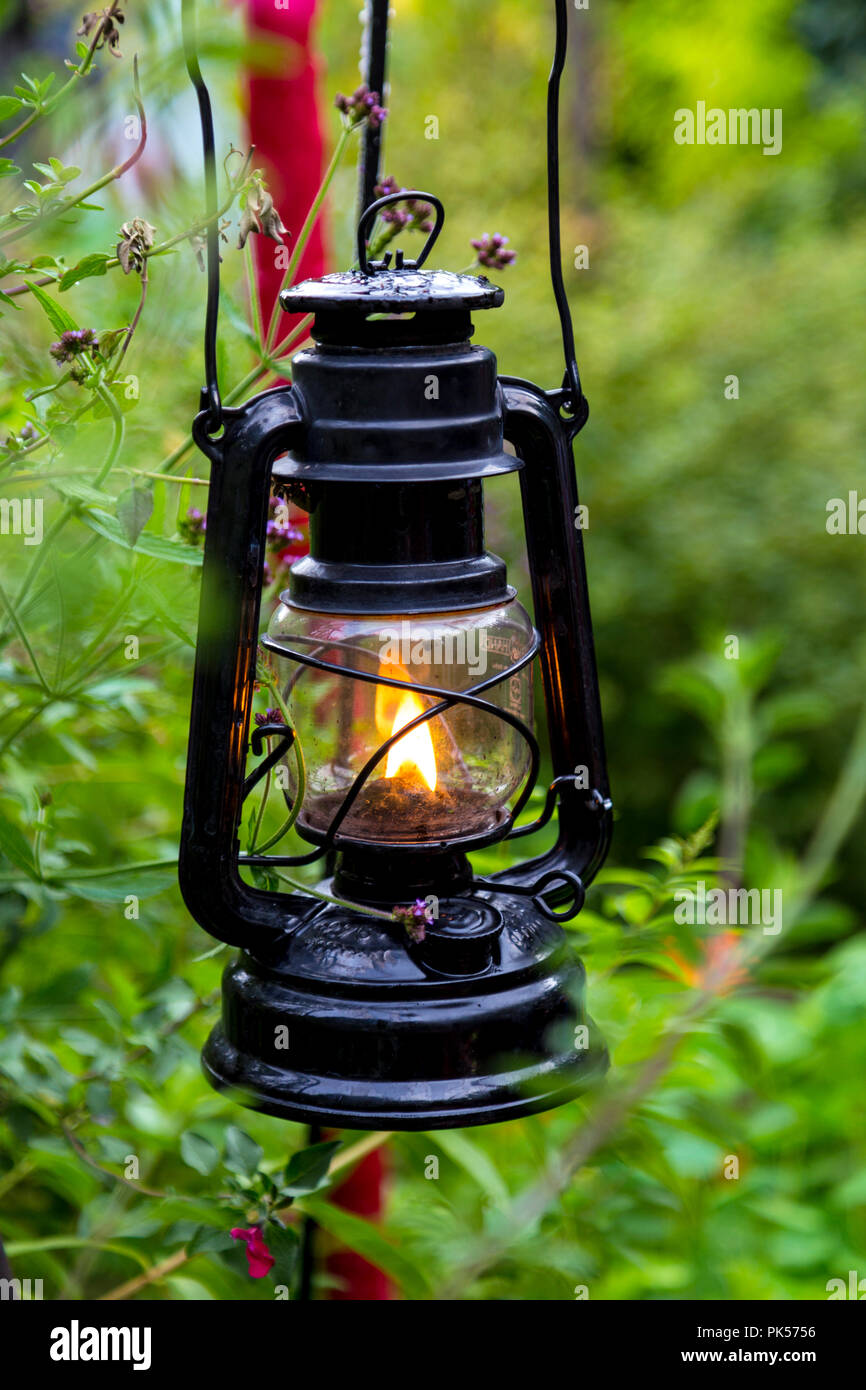 Hanging metal and glass old-fashioned garden lantern with a flame burning inside Stock Photo